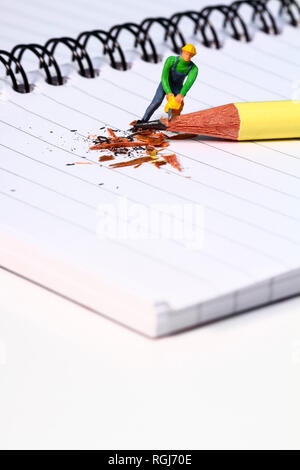 Diorama conceptuel image d'une figure miniature en affinant un crayon sur un carnet de notes Banque D'Images