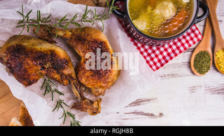Délicieux pilons de poulet rôti au romarin - les jambes et les épices dans des cuillères et de la soupe au poulet servi dans un bol traditionnel sur un sol en bois rustique backgroun Banque D'Images
