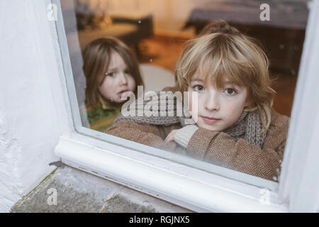 Portrait de jeune garçon à la fenêtre de sortie avec sa petite sœur dans l'arrière-plan Banque D'Images