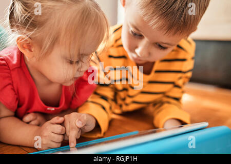 Frère et sa petite sœur se trouvant sur le plancher à la maison using digital tablet Banque D'Images