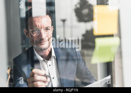 Businessman sitting in office, en utilisant les notes Banque D'Images
