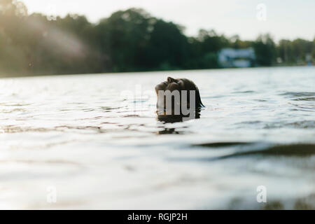 Femme flottant dans un lac au coucher du soleil Banque D'Images