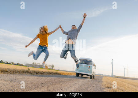 Couple exubérant de sauter sur un chemin de terre à camper van in rural landscape Banque D'Images