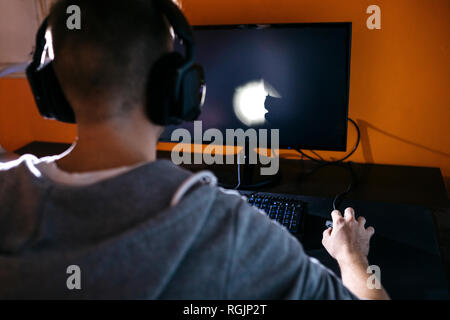 Jeune homme assis à son ordinateur, jouer à des jeux sur ordinateur Banque D'Images