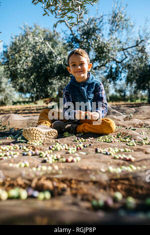 Portrait of smiling boy playing with olives dans oliveraie Banque D'Images