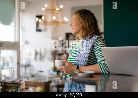 Jeune femme avec tasse de café et d'un ordinateur portatif dans un café Banque D'Images