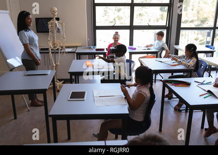 Vue latérale d'écolier à l'aide de casque de réalité virtuelle et de ses camarades et l'enseignant dans l'école élémentaire de classe Banque D'Images