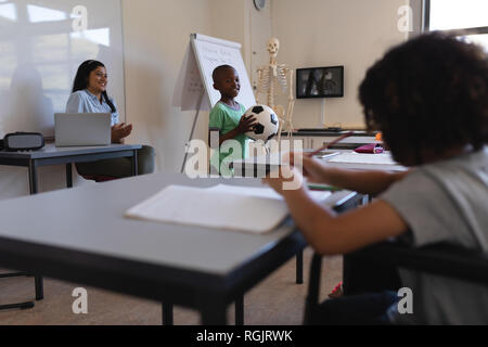 Smiling businesswoman holding football in classroom Banque D'Images
