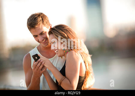 Jeune couple sourire en regardant un appareil portable d'informations. Banque D'Images