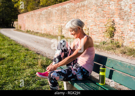 Smiling sportive senior woman sitting on a bench attacher ses chaussures Banque D'Images