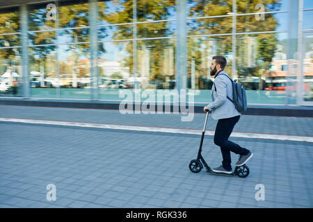 Businessman riding scooter le long office building Banque D'Images