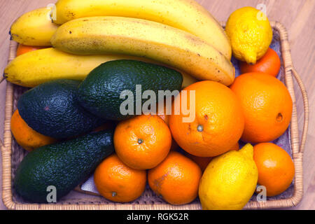 Nature morte avec fruits tropicaux : bananes, avocats, citrons, oranges et mandarines se situent sur un plateau en osier brun gros plan Vue de dessus Banque D'Images