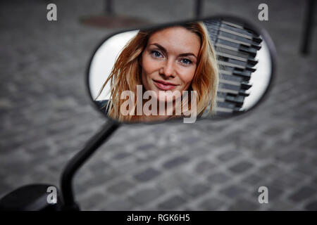 Portrait of smiling young woman reflète dans wing mirror d'une moto Banque D'Images