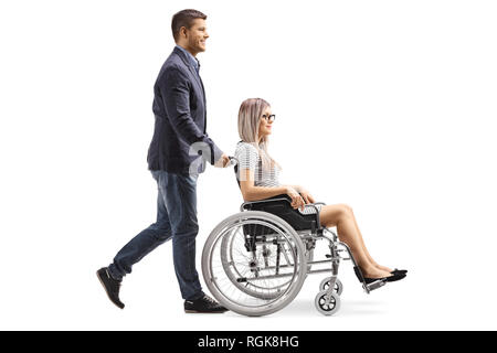 Profil de pleine longueur tourné d'un jeune homme poussant une jeune femme en fauteuil roulant isolé sur fond blanc Banque D'Images
