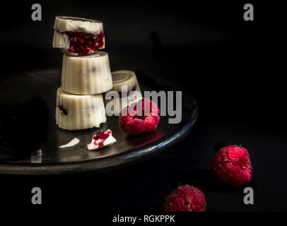 Chocolat blanc quatre truffes framboise rouge sur la plaque noire sur fond noir - photographie sombre Banque D'Images