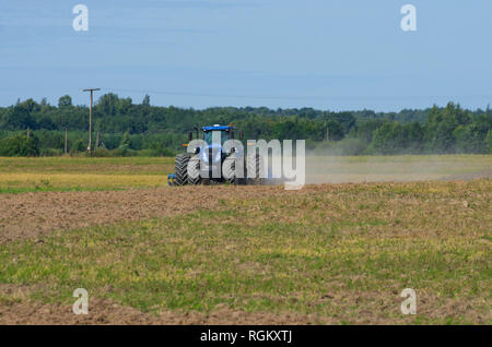 Vue avant du tracteur laboure le terrain avec une herse de fer dans la saison de labour avec la poussière tourbillonnante Banque D'Images