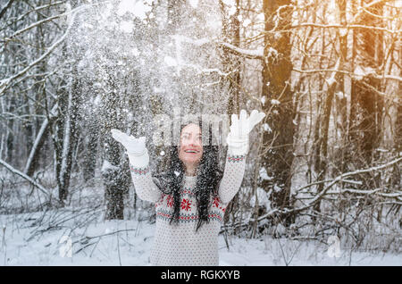 Une femme dans la forêt couverte de neige projette la neige avec ses mains sur l'arrière-plan les arbres. Plaisir d'hiver, relaxation, animation Banque D'Images