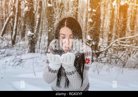 Une femme dans la forêt couverte de neige projette la neige avec ses mains sur l'arrière-plan les arbres. Plaisir d'hiver, relaxation, animation Banque D'Images