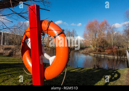 Une bouée de couleur orange vif à côté du bord de l'eau d'un lac dans un parc commercial. Banque D'Images