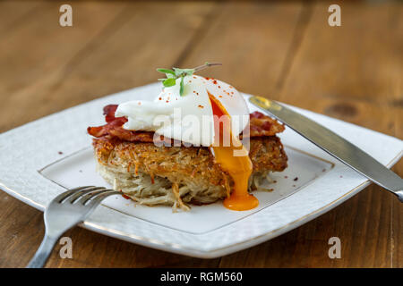 Rosti de pommes de terre, œuf poché avec runy jaune et bacon sur le dessus. Banque D'Images