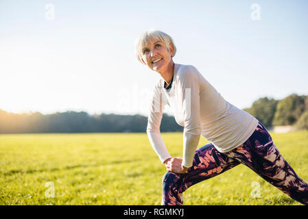 Smiling senior woman stretching on meadow rural Banque D'Images