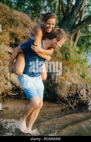 Happy man carrying girlfriend piggyback à un lac Banque D'Images