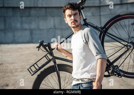 Jeune homme de banlieue transport fixie vélo au mur de béton Banque D'Images