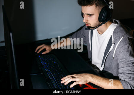 Jeune homme assis à son ordinateur, jouer à des jeux sur ordinateur Banque D'Images