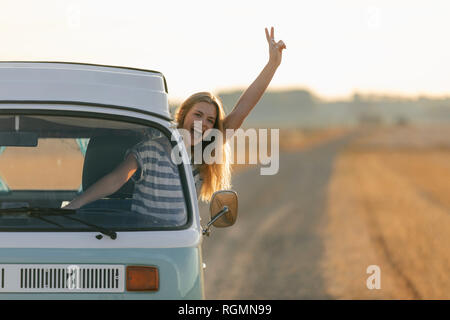 Jeune femme excité faisant signe de main victoire hors de la fenêtre de camping-car in rural landscape Banque D'Images