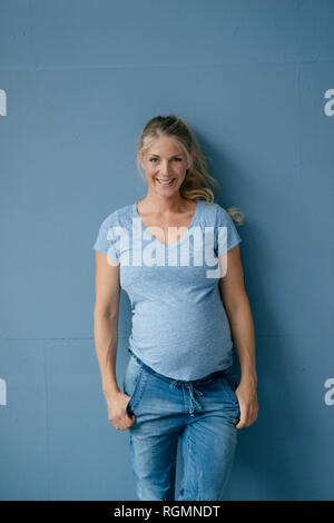 Portrait of smiling pregnant woman standing at mur bleu Banque D'Images