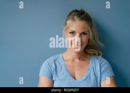 Portrait of smiling blonde woman standing at mur bleu Banque D'Images