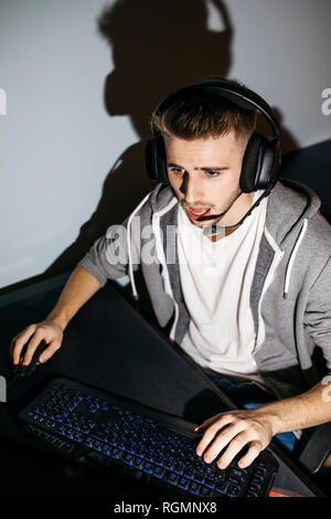 Jeune homme assis à son ordinateur, jouer à des jeux sur ordinateur Banque D'Images