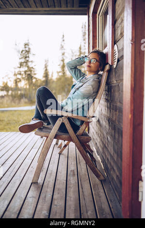 La Suède, la Laponie, portrait of young woman sitting on chair sur relaxant véranda Banque D'Images