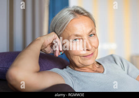 Portrait of smiling senior woman relaxing sur le canapé à la maison Banque D'Images