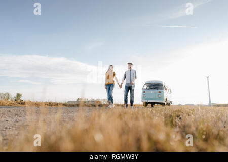 Jeune couple en train de marcher sur un chemin de terre à camper van in rural landscape Banque D'Images