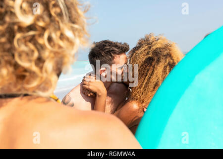 Couple sur la plage avec des amis, l'autre tkissing Banque D'Images
