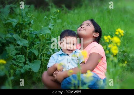 Une fille mignonne à en haut le ciel, exprimant l'espoir tout en tenant son petit frère dans ses bras, dans un champ avec des fleurs. Banque D'Images