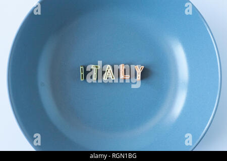 Le mot 'Italie' composé avec du vrai pâtes lettres dans le pavillon italien des couleurs dans un plat bleu. Banque D'Images