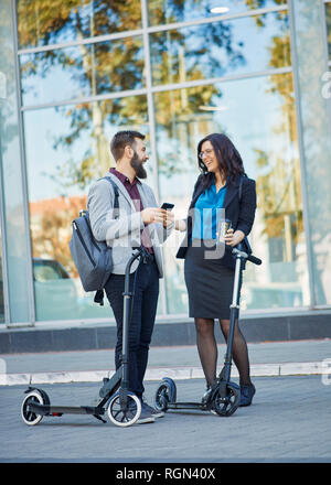 Happy businessman and businesswoman talking on scooters avec pavement Banque D'Images