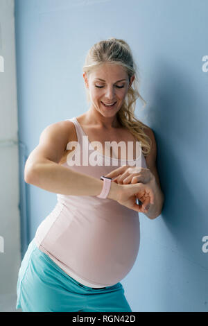 Portrait of smiling pregnant woman looking at smartwatch mur bleu Banque D'Images