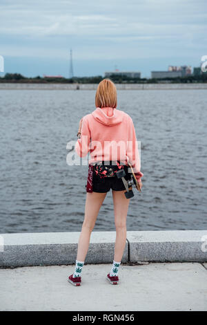 Young woman holding carver skateboard debout à la Riverside Banque D'Images