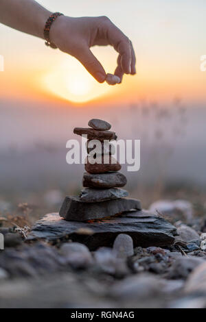 Close-up de la main de l'homme mise sur pierre cairn au coucher du soleil Banque D'Images