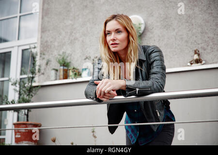 Certain jeune femme portant veste biker leaning on railing balcon Banque D'Images