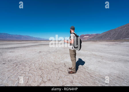 États-unis, Californie, la vallée de la mort, l'homme avec sac à dos et une bouteille d'eau dans le désert permanent à la recherche à distance Banque D'Images