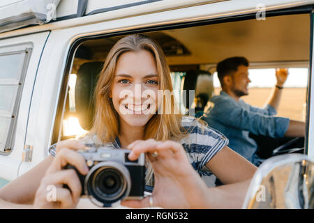 Portrait de femme heureuse avec caméra incliné vers l'extérieur de la fenêtre d'un camping-car avec l'homme au volant Banque D'Images