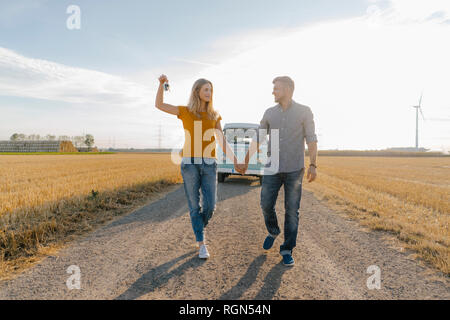 Jeune couple avec clé de voiture marcher sur un chemin de terre à camper van in rural landscape Banque D'Images