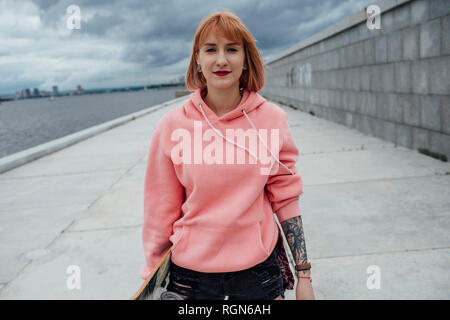 Portrait of young woman holding skateboard du riverside Banque D'Images