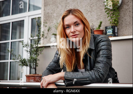 Portrait of young woman wearing biker jacket leaning on railing balcon