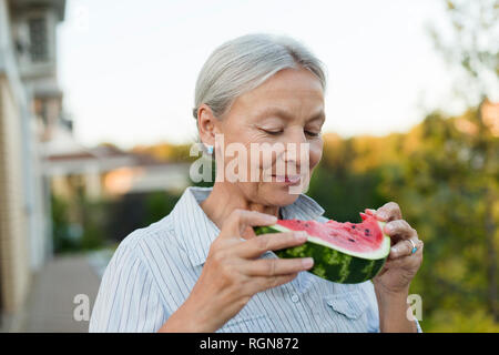 Portrait of senior woman eating watermelon slice dans le jardin Banque D'Images