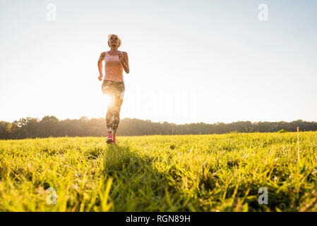 Senior woman running on meadow rural au coucher du soleil Banque D'Images